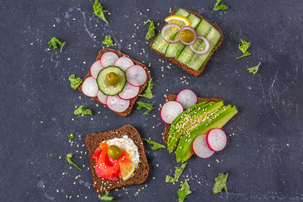 istock Appetizer, open sandwich with different toppings: salmon and vegetables (avocado, cucumber, radish) on dark background. Healthy eating. Organic and veggie food. Flat lay, copy space for text, 1273212949
