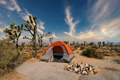 This image shows an empty camping tent in the middle of a remote desert landscape next to a fire pit.