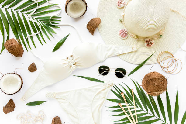 istock Feminine beige swimsuit beach accessories, tropical palm leaf branches, coconuts on white background with empty space for text. Flat lay, top view 1273217211