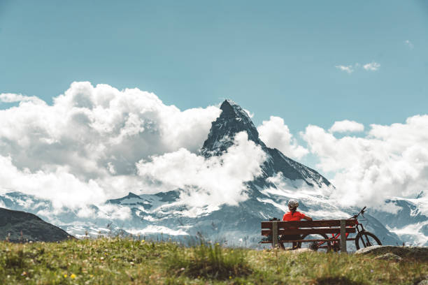 istock Matterhorn on a cloudy day and woman biker sitting on a bench 1273221912