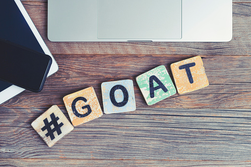 GOAT, Greatest of all time acronym. Laptop, digital tablet and mobile phone with a hashtag and the letters GOAT beside them. They are on a wooden background with copy space.