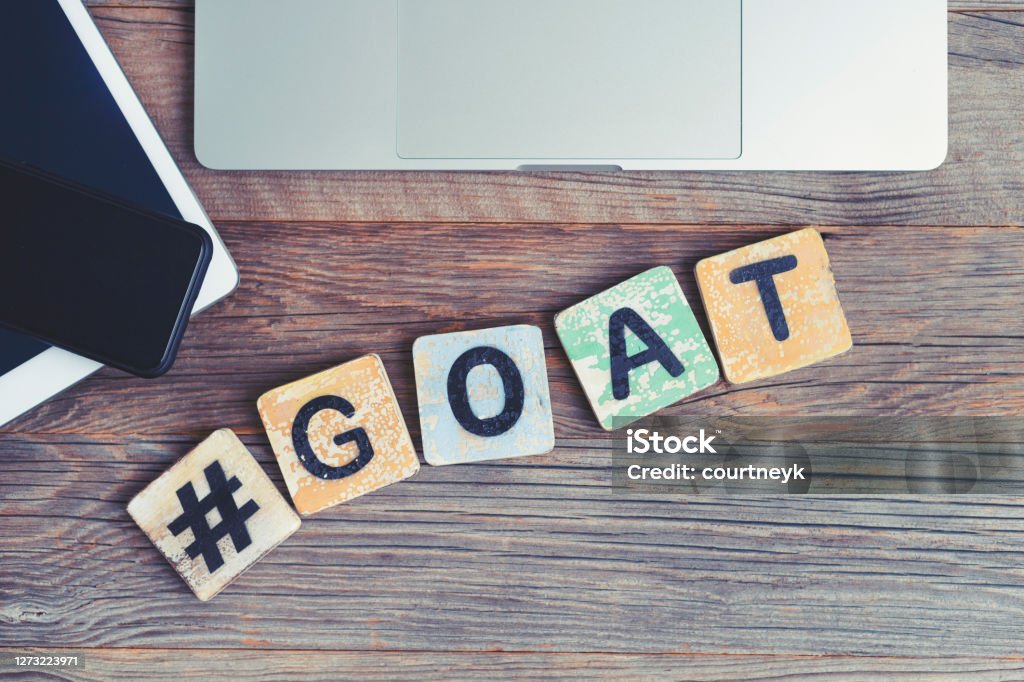 GOAT, Greatest of all time acronym. Laptop, digital tablet and mobile phone with a hashtag and the letters GOAT beside them. GOAT, Greatest of all time acronym. Laptop, digital tablet and mobile phone with a hashtag and the letters GOAT beside them. They are on a wooden background with copy space. Acronym Stock Photo