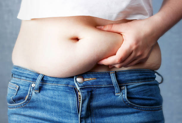 woman's hand holding excessive belly fat, overweight concept - torso women jeans abdomen imagens e fotografias de stock