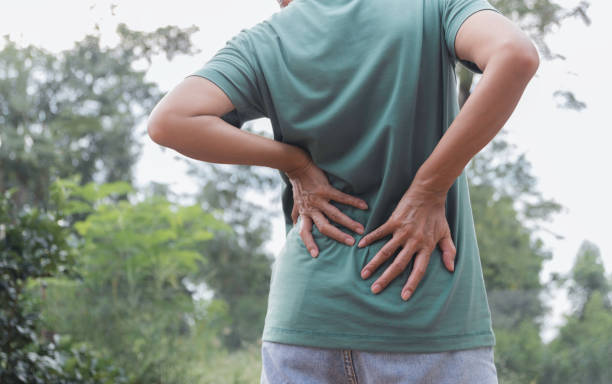 closeup hands of woman touching her back pain in healthy concept on nature background. - lower back pain imagens e fotografias de stock