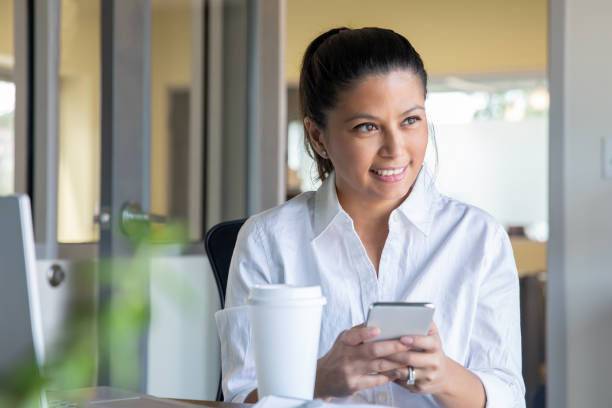 istock Woman uses smart phone and drinks morning coffee while sitting in her office 1273235978