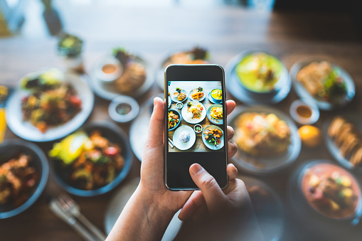 Person standing next to food table and taking photos with phone before eating it.