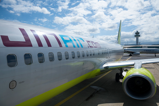 A Virgin Australia Boeing B737-8FE plane, registration VH-VOK, parked at a gate of the domestic terminal of Sydney Kingsford-Smith Airport. One of the cargo doors is open for loading. This image was taken inside the terminal on a sunny afternoon on 1 April 2024.