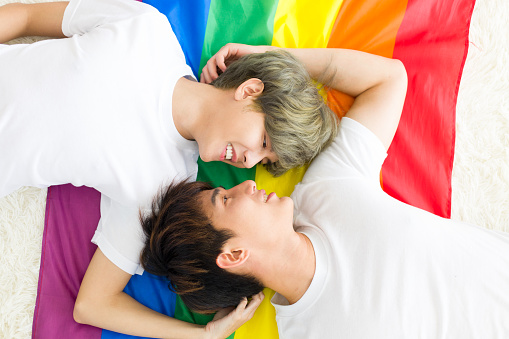 Asian male homosexual or gay couples lying down on a rainbow flag, and both of them are making eye contact together. Concept of LGBTQ pride.