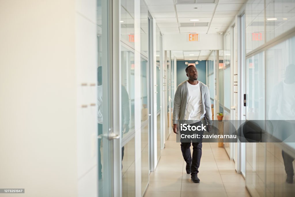 Relaxed Black Freelancer Walking in Miami Coworking Office Full length front view of man in mid 20s wearing casual clothing and approaching camera while walking in office hallway carrying laptop. Walking Stock Photo
