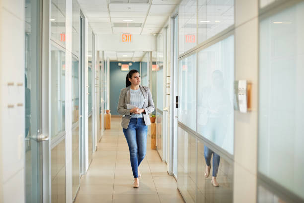 Young Hispanic Businesswoman Walking in Coworking Office Full length front view of casually dressed woman in mid 20s holding digital tablet and approaching camera while walking in Miami office hallway. approaching stock pictures, royalty-free photos & images