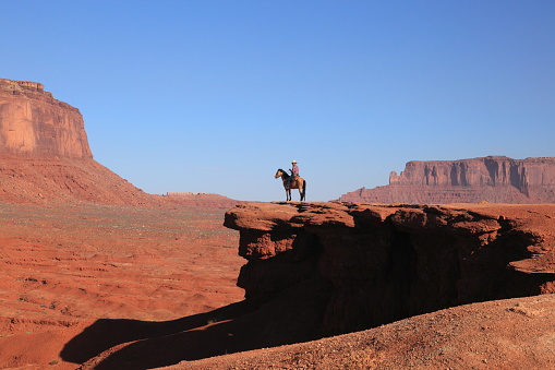 Western Cowboy riding on Horse  from John Ford's Point overlook in Monument Valley Tribal Park with the mittens and Merrick Butte in Arizona, USA