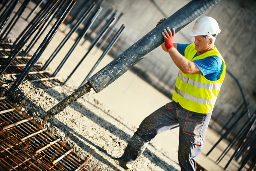 Closeup of a construction worker guiding a hose from a concrete pump and filling rebar mesh. This is fast setting concrete, takes three hours to dry.