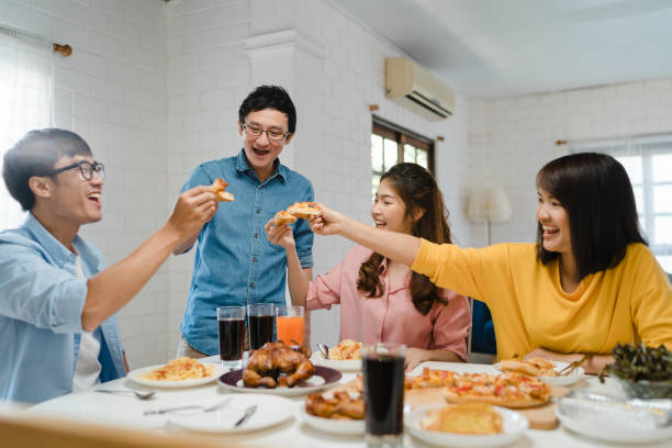 Asia family party eating pizza food and laughing enjoying meal while sitting at dining table together at house. Happy young friends group having lunch at home. Asia family party eating pizza food and laughing enjoying meal while sitting at dining table together at house. Celebration holiday and togetherness. Reach out to friends stock pictures, royalty-free photos & images