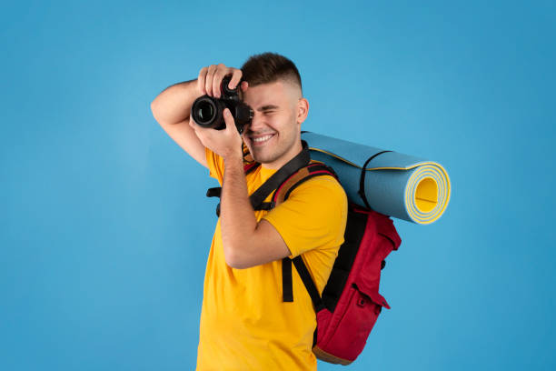 istock Happy young traveler with backpack and camera ready to take photos on blue background 1273274416
