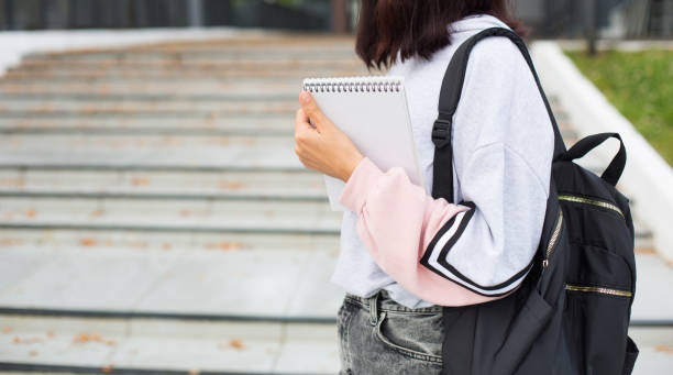 istock A female student with a black backpack and a notebook in her hands stands on the steps in front of the Institute. Higher education, the beginning of the school year, back to school. Copyspace 1273274677