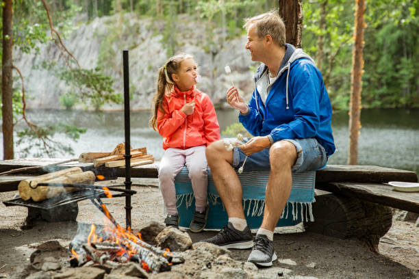 el hombre y su hija pequeña teniendo barbacoa en el bosque - camping family vacations eating fotografías e imágenes de stock