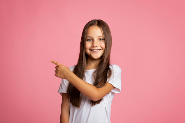 istock Wow, cool. Smiling little child points with finger behind back, to empty space 1273275749