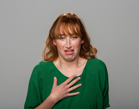 Young woman feeling displeased standing against grey background.