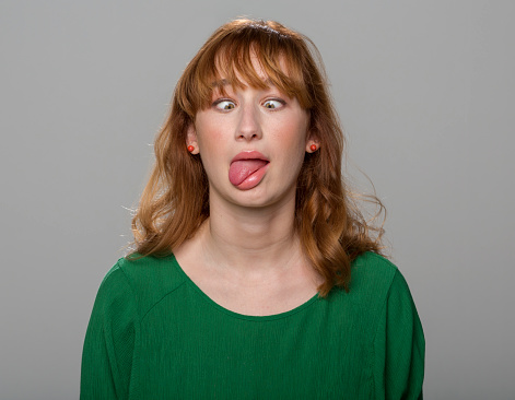 Young woman making squint while standing against grey background.
