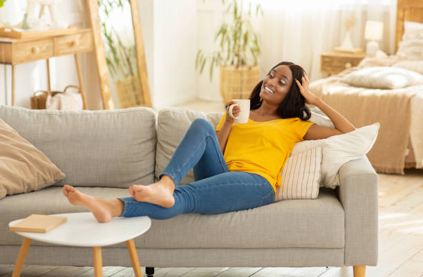 belle jeune femme noire détendant sur le sofa avec la tasse de café à la maison - coffee cup black coffee isolated photos et images de collection