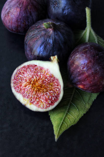 una rebanada de higo púrpura con una hoja verde sobre un fondo oscuro de cerca - fig fotografías e imágenes de stock