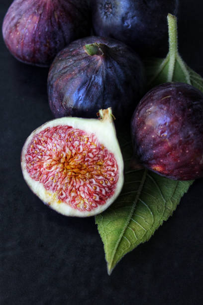 A slice of purple Fig with a green leaf on a dark background close-up A slice of ripe figs with a green leaf on a dark background close-up.Texture or background fig photos stock pictures, royalty-free photos & images