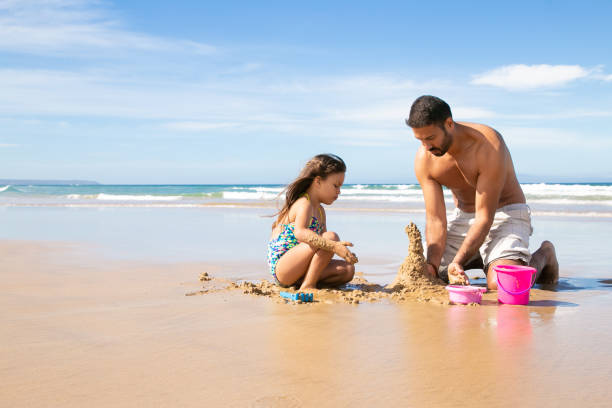 istock Focused handsome dad and little daughter building sandcastle 1273283421