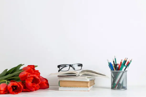 Photo of Books, red tulips and school supplies on a white background. The concept of a postcard for teacher's day. Copy space.