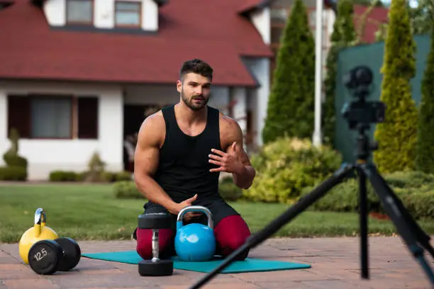 A fitness trainer and workout influencer is recording an inspirational training video outdoors.