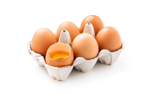 Front view of a half a dozen eggs carton isolated on white background. One of the eggs is broken and the yolk can be seen. Studio shot taken with Canon EOS 6D Mark II and Canon EF 100 mm f/ 2.8