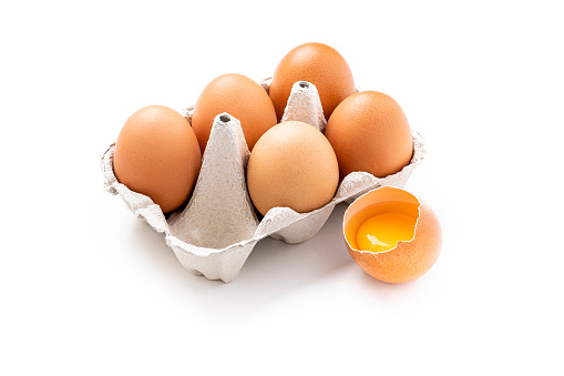 High angle view of a half a dozen eggs carton isolated on white background. One of the eggs is broken and outside the carton and it yolks can be seen. Studio shot taken with Canon EOS 6D Mark II and Canon EF 100 mm f/ 2.8