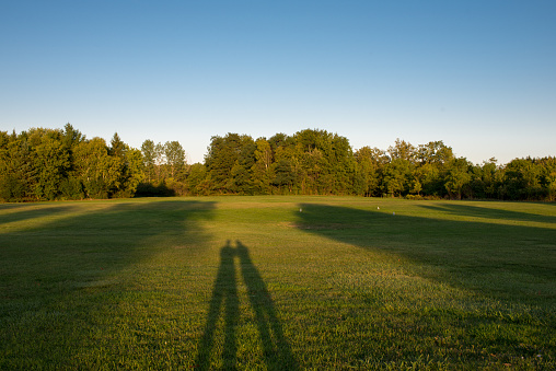 Shadow of a young adult man walking on imaginative white line tightrope on green grass.