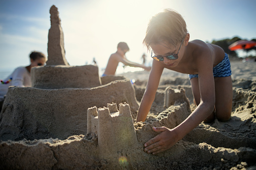 Three kids are having fun building a huge sandcastle on a beach on a sunny summer day. \nNikon D850