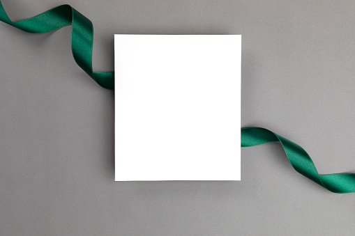 White blank empty greeting card on gray background wrapped with a green colored ribbon.