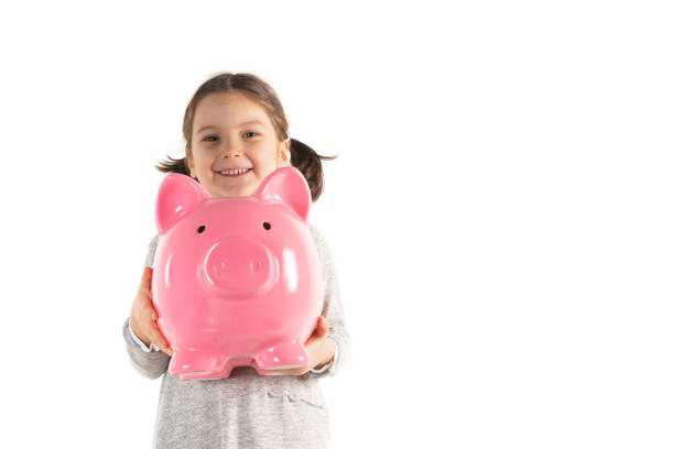 Toddler is holding big pink piggybank and is looking at camera with a toothy smile in front of pure white background.