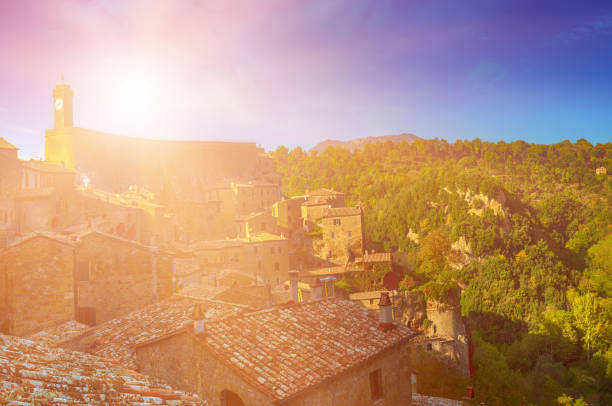 Sorano - tuff city in Tuscany. Italy. View to the clock tower and roofs of the town with green trees and blue sky.