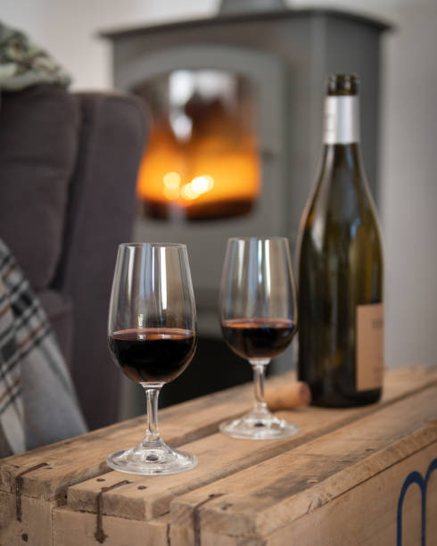 two wine glasses in front of fireplace red wine, lit fireplace, wooden coffee table and a knit blanket on the sofa hygge photos stock pictures, royalty-free photos & images