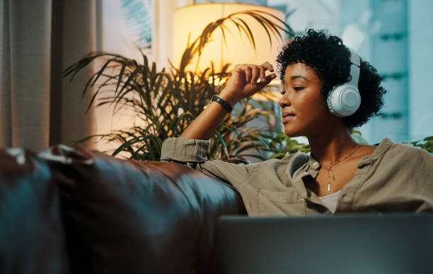 Feeling bored? Technology can take care of that Shot of a young woman wearing headphones while sitting at home with her laptop headphones stock pictures, royalty-free photos & images
