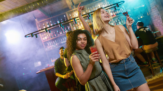 Attractive young women getting drunk, posing with cocktail in their hands. Friends celebrating, having fun in the bar. Selective focus. Web Banner