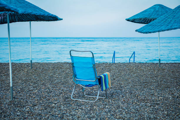 A blue beach chair by the sea with towel  on a pebble beach between four beach umbrellas