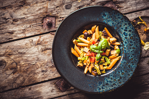 Vegan Low Carb Lentil Pasta Loaded with important proteins, with Veggies and Tofu served outdoors on a rustic wooden table