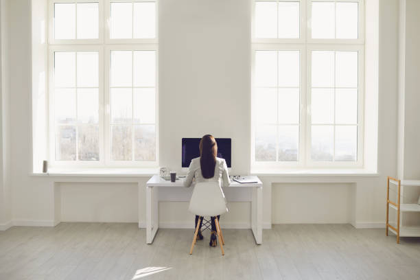 istock White bright spacious office. Back view of a female employee working at a desk with a computer in a white office with windows. 1273312499