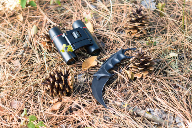istock karambit knife and binoculars between fir cones on the ground in the forest 1273314832