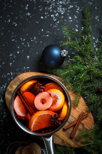 Steel pan with cooked mulled wine with cinnamon, apple and oranges surrounded by fir branches and christmas balls