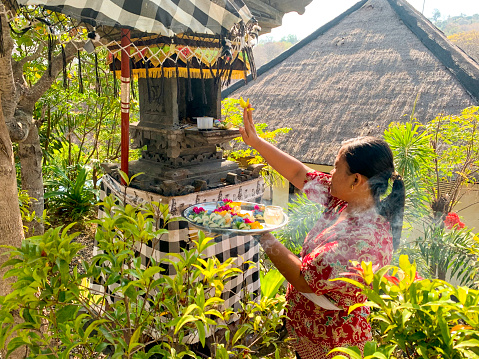 Side view of an Asian woman placing offerings known as 'canang sari' in the family temple. This is part of her morning ritual routine.