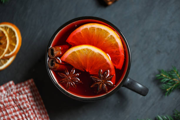 Top view of a glass of mulled wine Black mug with bright red mulled wine, two slices of orange, cinnamon and star anise on a dark gray table mulled wine photos stock pictures, royalty-free photos & images
