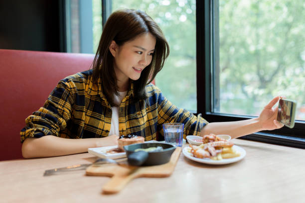 Young Asian woman using a smart phone to take a selfie with her food. Young Asian woman using a smart phone to take a selfie with her food. chinese ethnicity china restaurant eating stock pictures, royalty-free photos & images