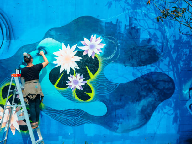 Female mural artist at work Female mural artist creating art on the wall exterior in public park in the city. street art stock pictures, royalty-free photos & images