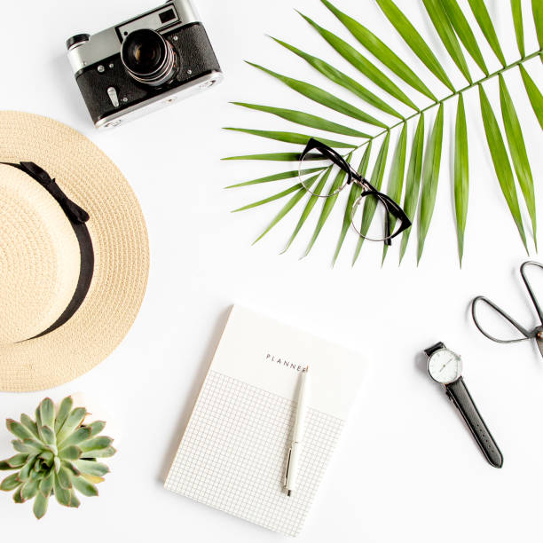 istock Top view home office desk. Workspace with straw hat, glasses, retro camera, notepad and tropical palm leaf on white background. Flat lay, top view 1273323073