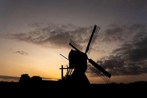 Silhouette of a traditional Dutch windmill against the red orange light of the rising or setting sun in a rural landscape